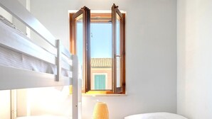 A room with a bunk bed, a bedside lamp, and a window with a view of a building with green shutters. - 2 bedroom nice home in Marina di Modica (Marina di Modica)