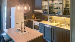 Una cocina moderna con una isla central, horno empotrado, lavavajillas y pileta. Luces colgantes sobre la isla.