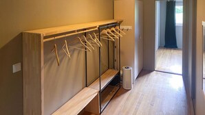 Un pasillo con un banco de madera, un tendedero con ropa y un altavoz blanco en el suelo.