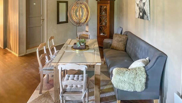 Un comedor con mesa y sillas de madera, un sofá gris y una lámpara colgante decorativa.