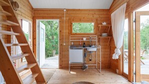 A wooden cabin interior with a kitchen area, a window, and a door leading outside.