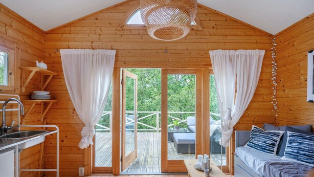 A cozy wooden cabin with a kitchen, dining area, and a large sliding glass door leading to an outdoor deck.
