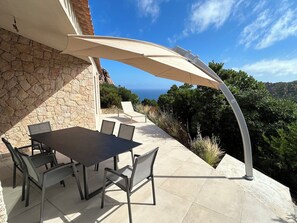 An outdoor patio with a table and chairs, a stone wall, and a view of the ocean. - Luxury villa with stunning sea view and heated infinity pool in Costa Paradiso (Costa Paradiso)
