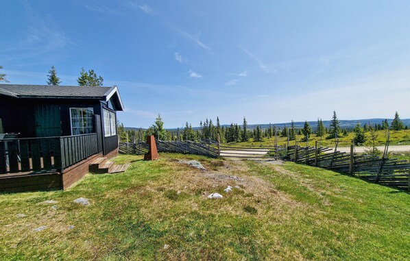 A cabin with a deck, surrounded by a forest and a view of distant mountains.