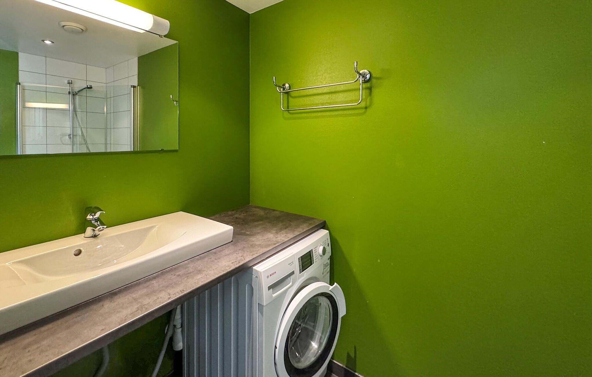 Une salle de bain avec un lavabo, un miroir, des murs verts et un lave-linge.