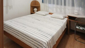 Ein ordentlich bezogenes Bett mit Streifenmuster, ein hölzerner Kopfteil, ein Nachttisch mit Lampe und ein Stuhl mit grün-weißem Muster.