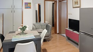 Ein kompakter Wohnraum mit Esstisch, Stühlen, einer Couch, einem Fernseher und einem Kühlschrank.