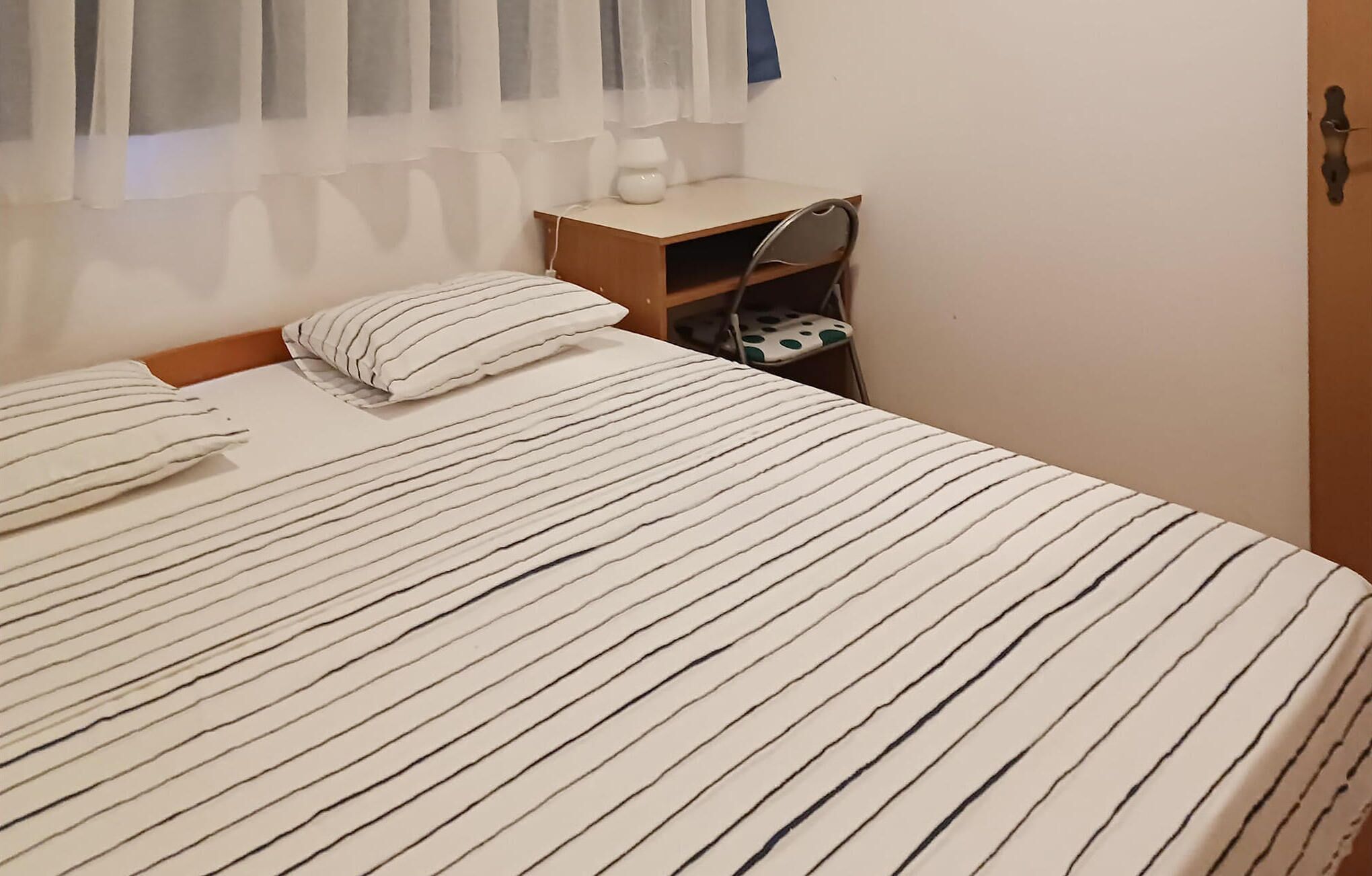 A bed with striped bedding, a bedside table with a lamp, and a chair with a polka dot cushion.