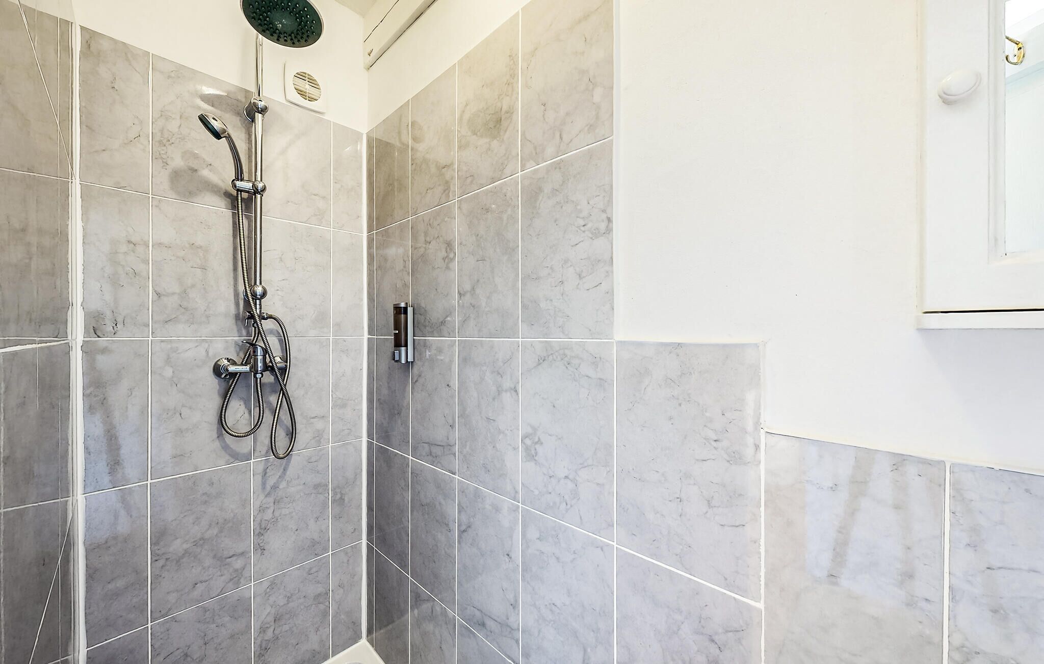 A shower with a handheld showerhead and a wall-mounted control panel.
