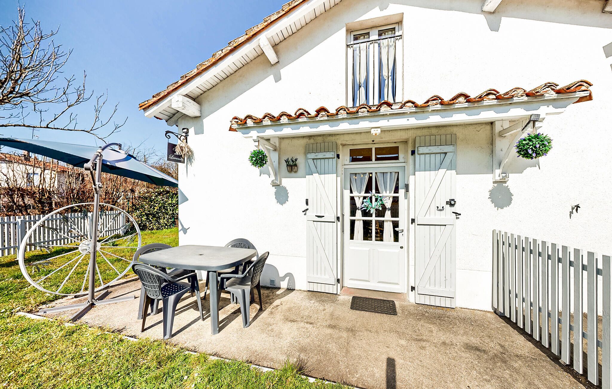 Un bâtiment blanc avec un toit recouvert de tuiles, une porte blanche dotée d’une fenêtre et un petit patio avec une table et des chaises.