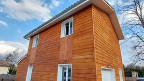 Une maison en bois à deux étages, avec un toit à pignon, des encadrements de fenêtres blancs et une porte de garage.