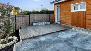 Une terrasse en bois bordée de pierres, avec un banc et une petite fenêtre.