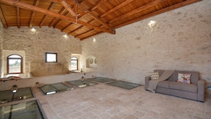 Una habitación amplia con pared de piedra, vigas de madera en el techo, una mesa de cristal y un sofá.