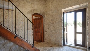 Una habitación con paredes de piedra, una escalera de madera, una puerta de madera y un ventanal grande.