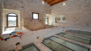 Una habitación con paredes de piedra, techo de madera, una ventana y un pequeño estante con platos decorativos.