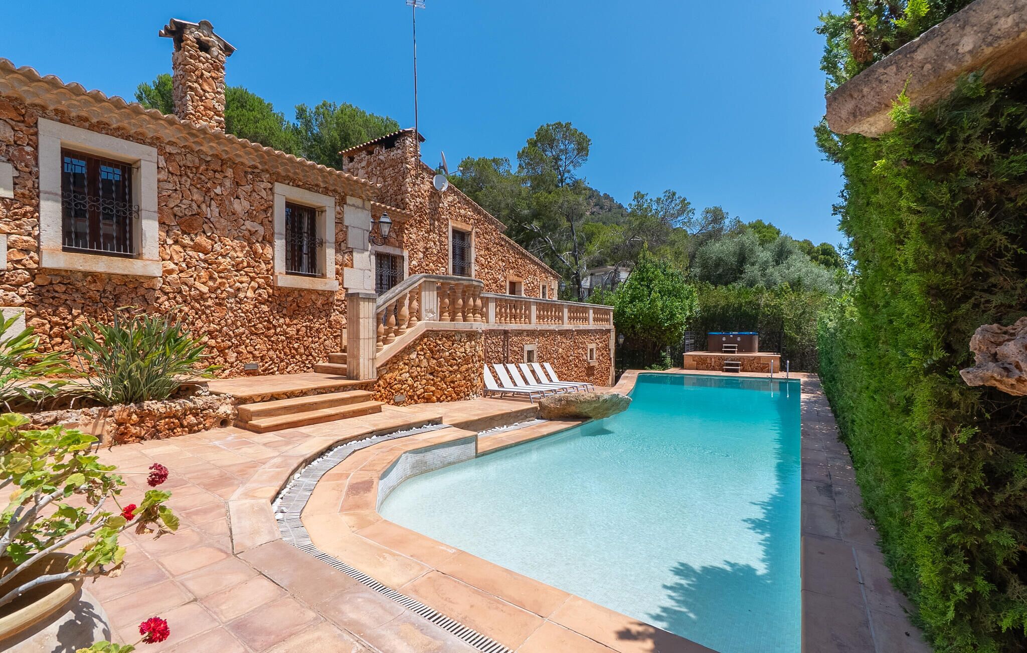 Uma casa de pedra com piscina, escadas para uma varanda e vista para o verde ao redor.