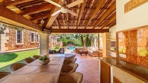 An outdoor patio with a long table and wicker chairs, a ceiling fan, and a stone wall. - Amazing home in Son Servera (Son Servera)