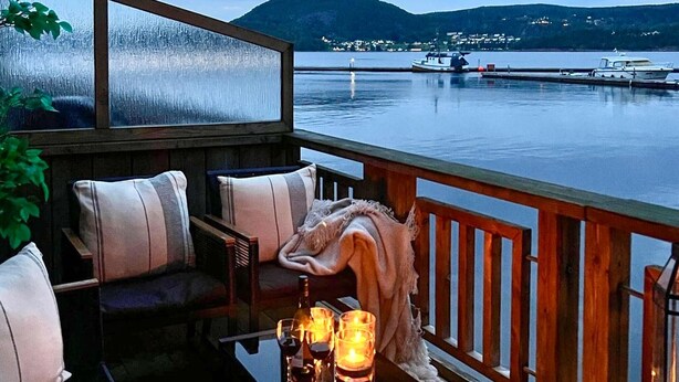 Uma área de estar aconchegante ao ar livre, com vista para um lago tranquilo e colinas distantes.