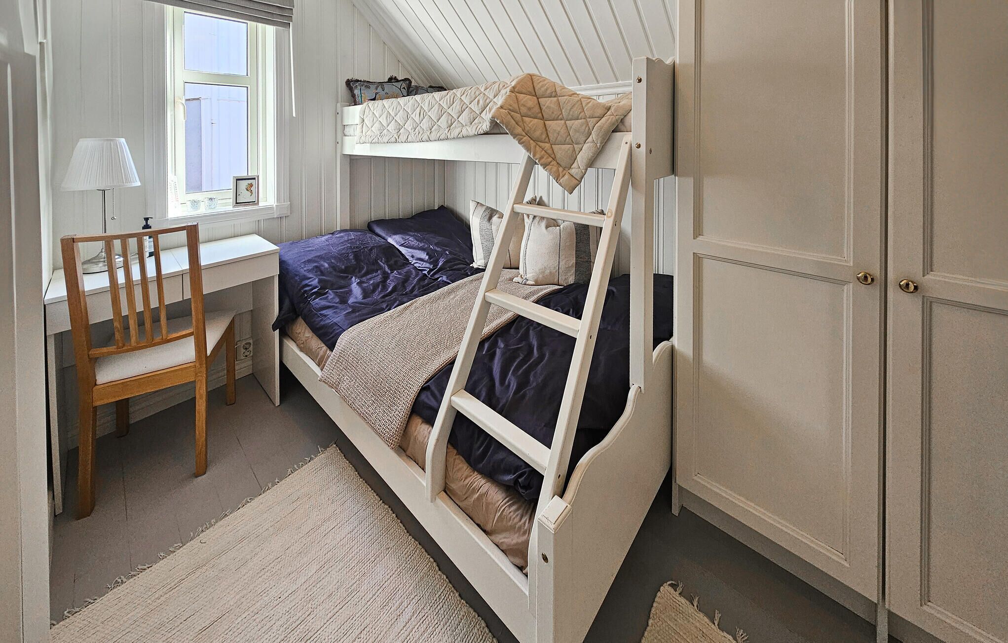 Een kleine slaapkamer met een stapelbed, een bureau en een stoel.