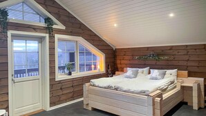 A bedroom with a wooden sloped ceiling, a large bed with white bedding, a window with a view, and a small table with a plant. - Beautiful home in Charlottenberg (Charlottenberg)