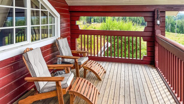 A wooden deck with two rocking chairs and a table, overlooking a green landscape. - Beautiful home in Charlottenberg (Charlottenberg)