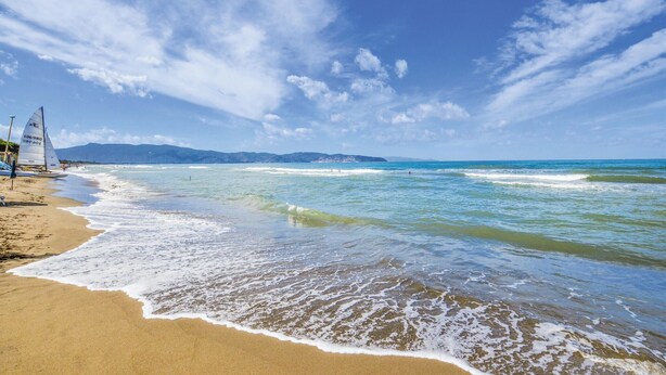 A beach with clear skies, gentle waves, and a sailboat on the sand.
