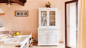 A dining area with a white table set for two, a white cabinet with glass doors, and a framed picture on the wall.
