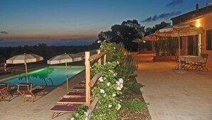 A swimming pool with lounge chairs and umbrellas, a wooden pergola with climbing plants, and a patio area with a table and chairs.