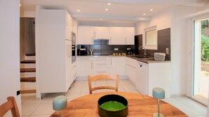 Een moderne keuken met witte kasten, een eettafel met stoelen en uitzicht op de buitenlucht door een schuifdeur.
