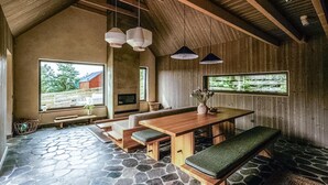Een rustiek interieur met een stenen vloer, houten meubels en grote ramen met uitzicht op het landschap.