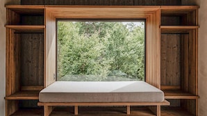 Een raamzitplaats met een kussen, omlijst door houten panelen, met uitzicht op een weelderig groen landschap.