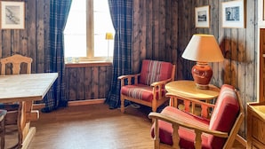 A cozy room with wooden walls, a wooden dining table, a red upholstered chair, a wooden armchair, and a table lamp. - Awesome apartment in Rauland (Rauland)