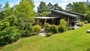 Una casa moderna con un porche cubierto, rodeada de exuberante follaje y plantas en flor.