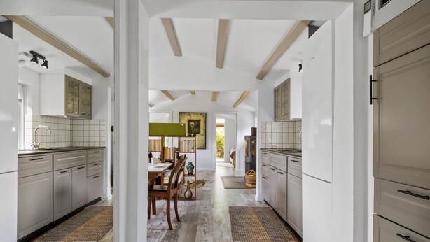 Una cocina moderna con armarios blancos, un comedor con mesa y sillas de madera, y vistas a una sala de estar.