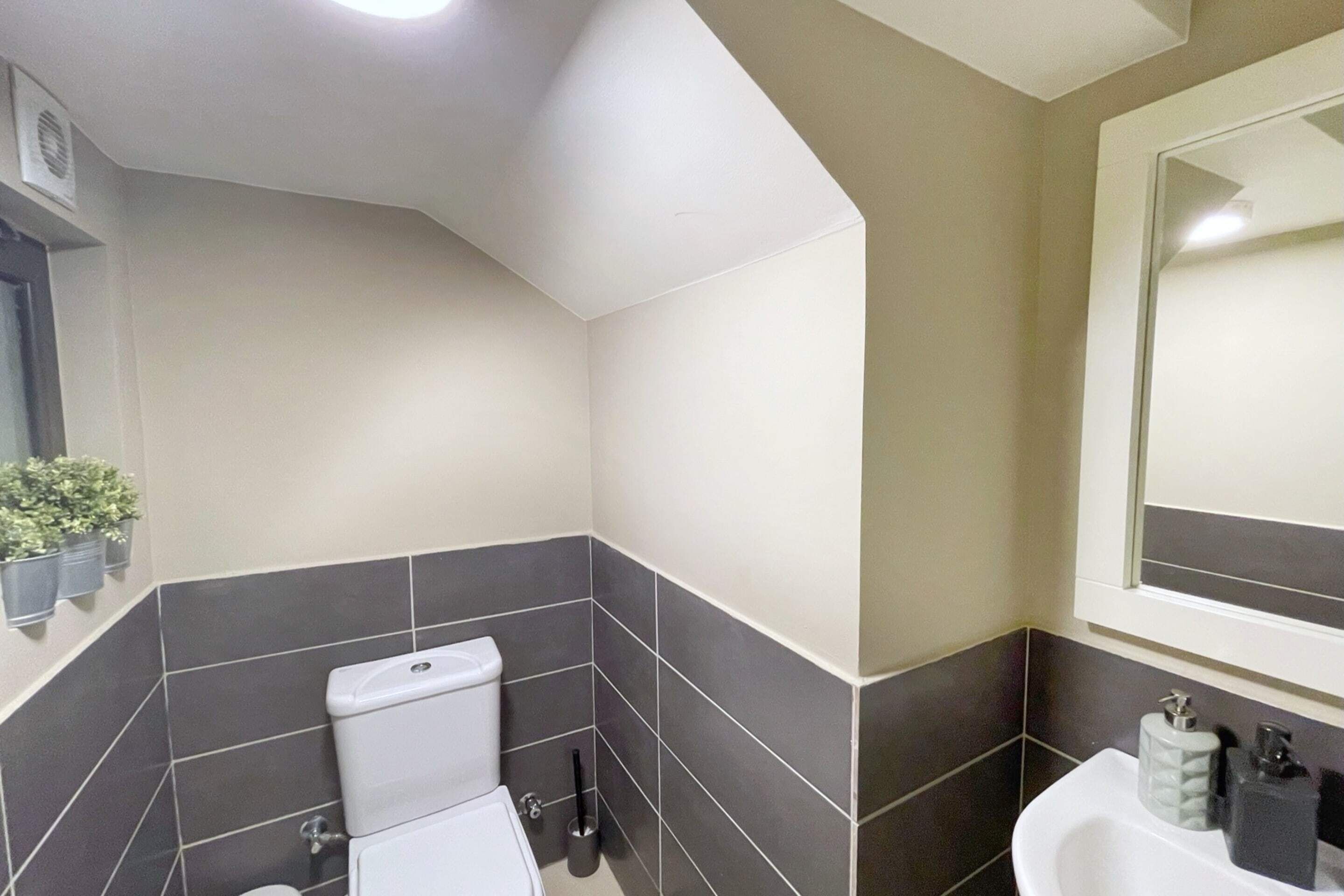 A bathroom with a white toilet, dark grey tiles, a white sink, and a mirror above the sink.
