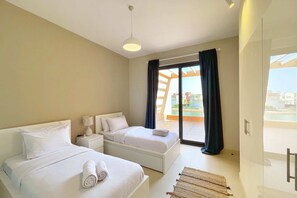 Une chambre d’hôtel moderne avec deux lits, une table de chevet, une lampe et une vue sur l’extérieur grâce à une porte vitrée.