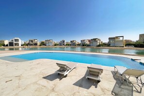 A swimming pool with lounge chairs and a view of modern buildings. - Xuru Stays I Homey 3 BDR Townhouse @ Tawila El Gouna (El Gouna)