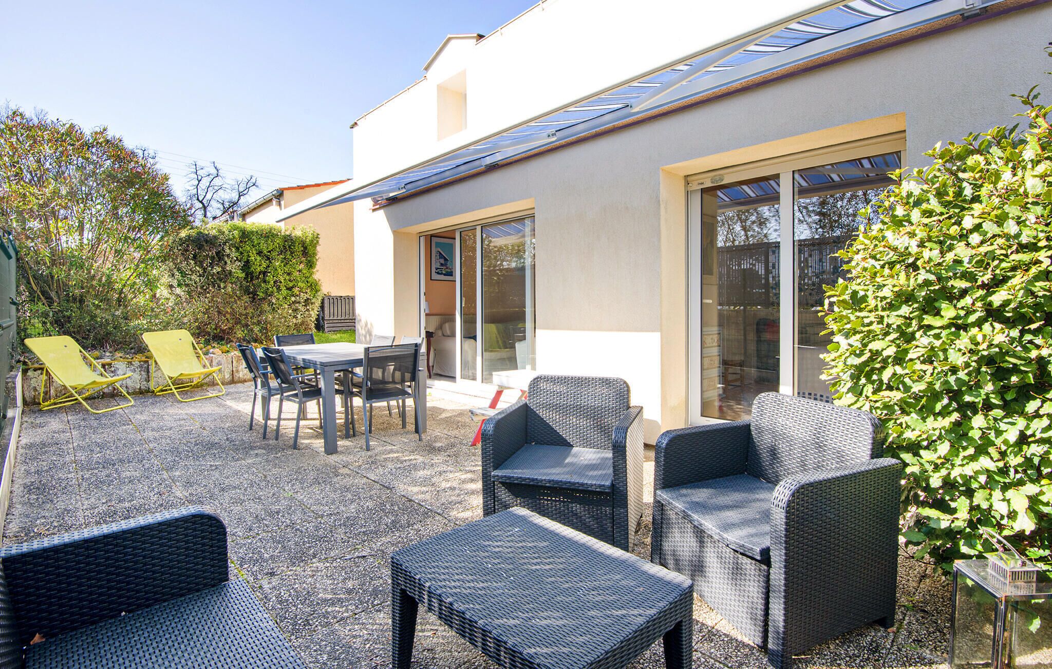 A patio area with outdoor furniture, including chairs and a table, and a glass door leading to a covered space.