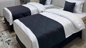 Habitación de hotel con dos camas, un ventanal con cortinas, un equipo de aire acondicionado y un adorno en la pared.