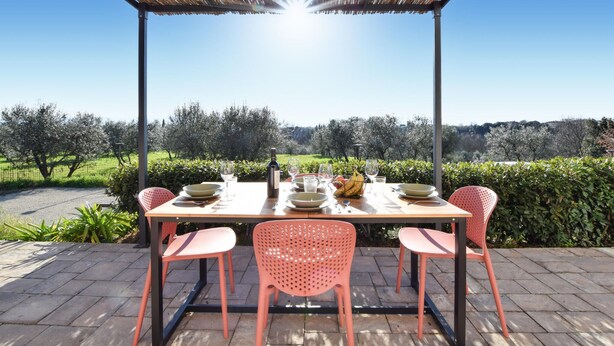 An outdoor dining area with a table set for four, surrounded by pink chairs, under a pergola with a view of a green landscape. - Nice apartment in Terranuova Bracciolini (Terranuova Bracciolini)