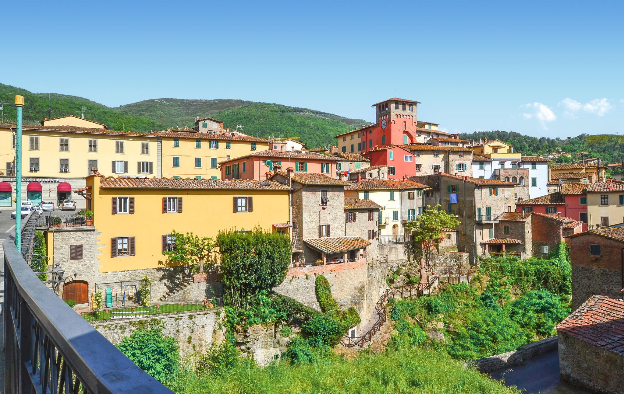 A historic town with colorful buildings, a prominent tower, and a stone wall with a spiral staircase.