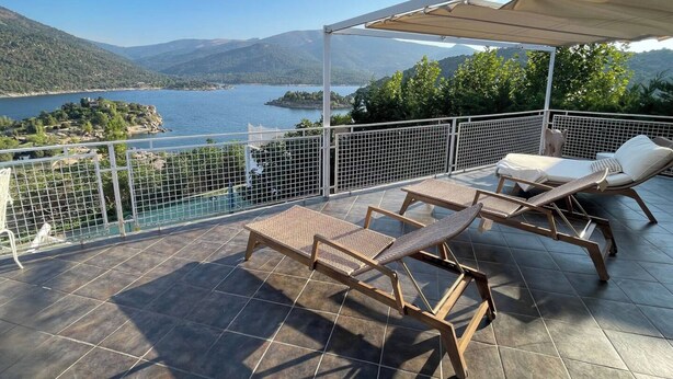 En terrass med två solstolar, en pergola och utsikt över en sjö och berg.