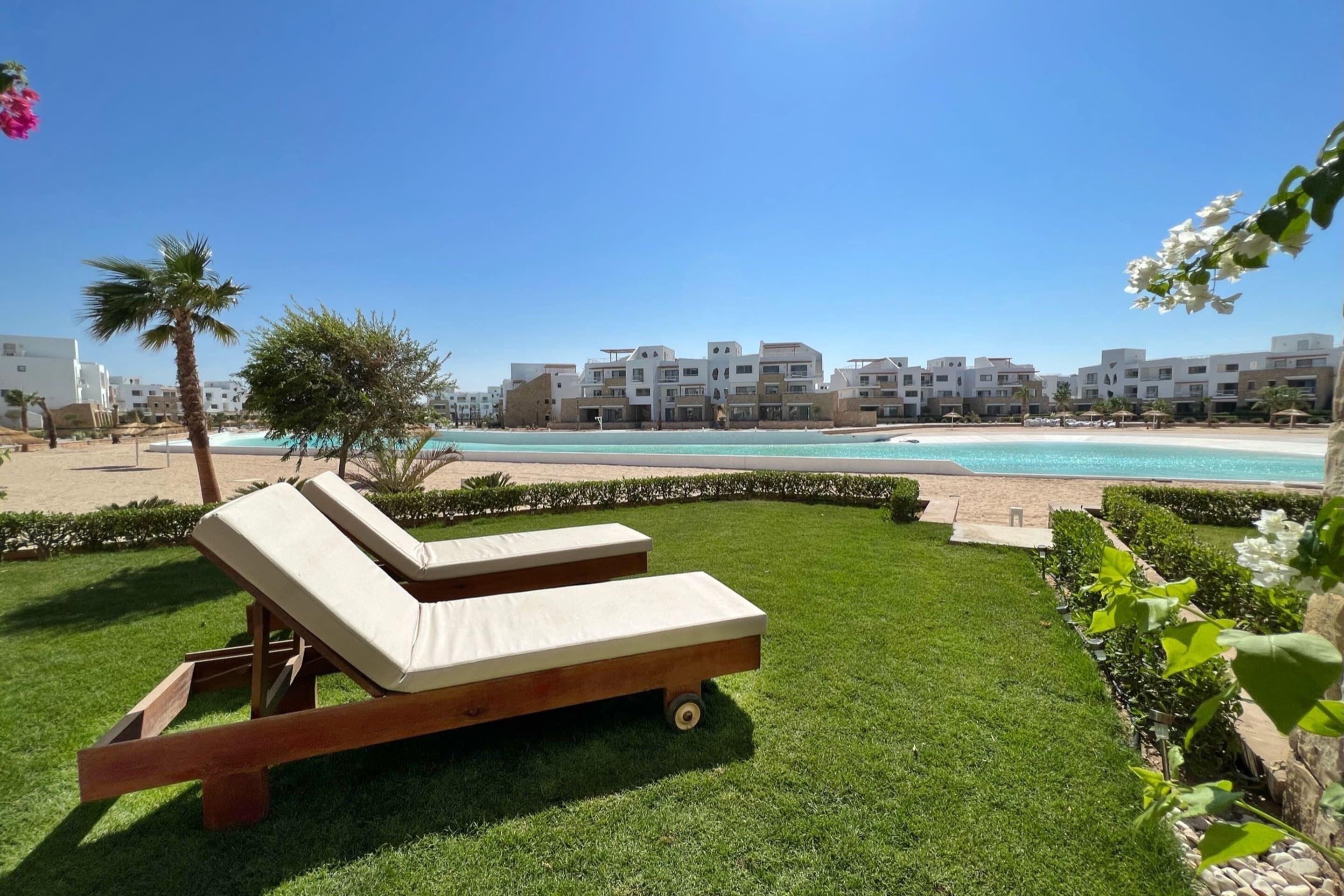 Un área junto a la piscina con dos sillones de descanso, vistas despejadas a la playa y una hilera de edificios al fondo.