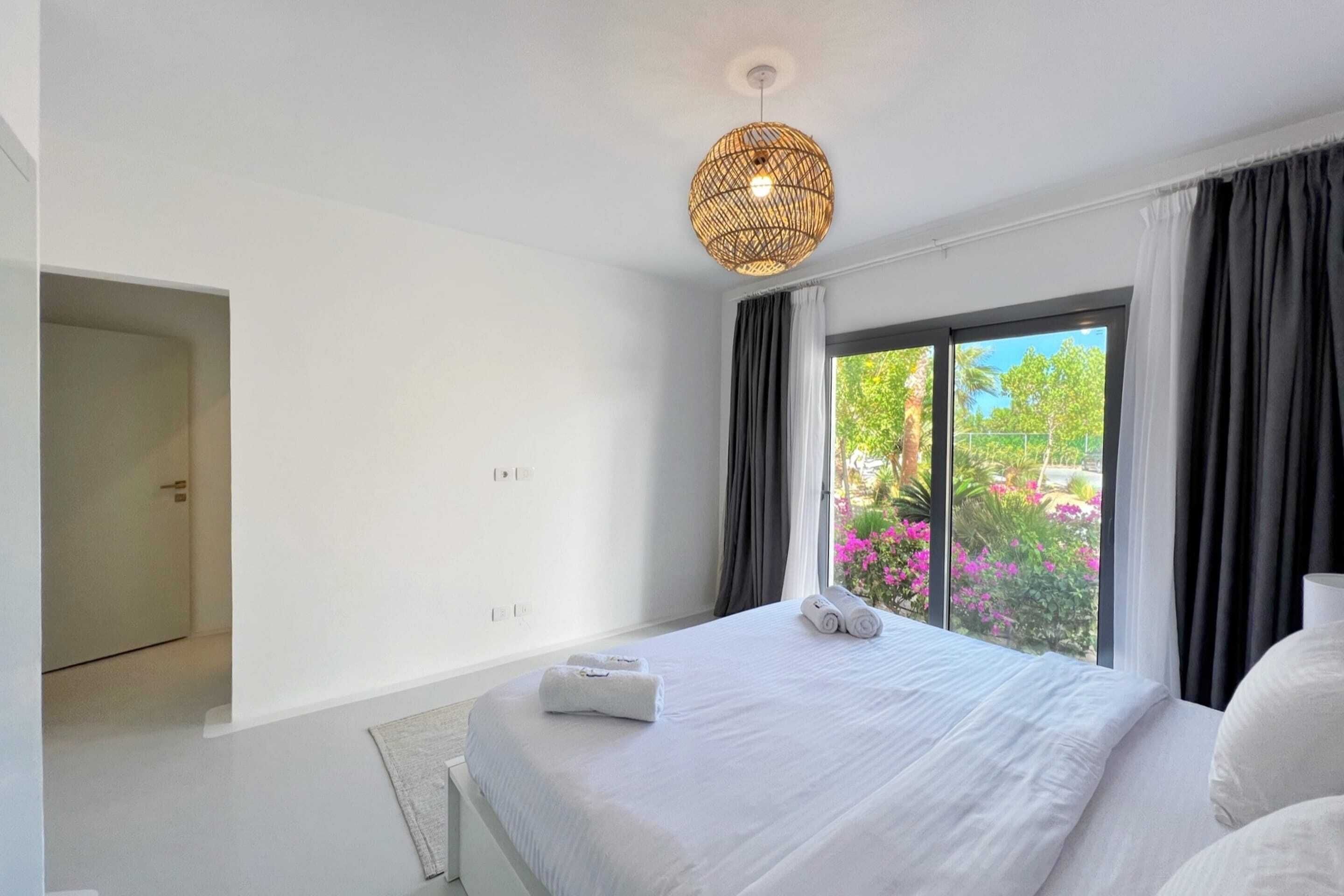 Une chambre d’hôtel moderne avec un grand lit, un luminaire suspendu et une vue sur la verdure.