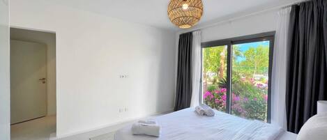 Une chambre d’hôtel moderne avec un grand lit, un luminaire suspendu et une vue sur la verdure.