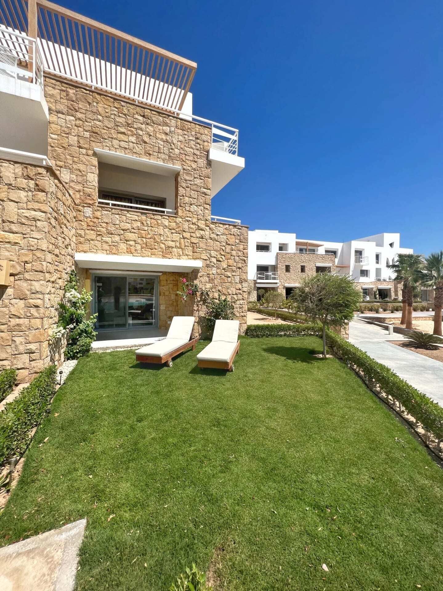 A modern building with stone facade, a well-maintained lawn, and two lounge chairs.