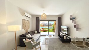 Una sala de estar moderna con sofá, sillón, mesa de centro y una zona de cocina con lavamanos y encimera.