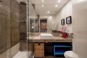 A modern bathroom with a glass-enclosed shower, a white sink, and a blue storage unit. - Chiado Mercy I (Lisbon)