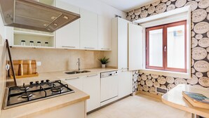 A modern kitchen with white cabinets, a gas stove, a sink, and a window with a wooden frame. - Chiado Mercy I (Lisbon)