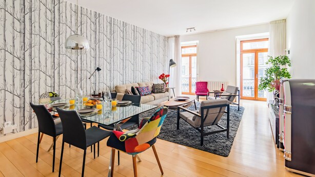 A modern living room with a dining area, featuring a sofa, chairs, a coffee table, and a large window with curtains. - Chiado Mercy I (Lisbon)